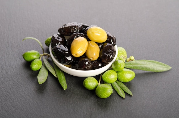 Olives noires et vertes mélangées dans le bol en porcelaine sur pierre grise