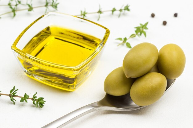 Olives vertes dans une cuillère en métal. L'huile d'olive dans un bocal en verre. Gros plan