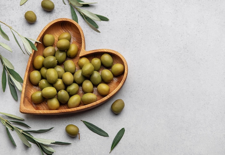 Photo des olives vertes fraîches exposées sur un bol en forme de cœur en bois avec des branches d'olive