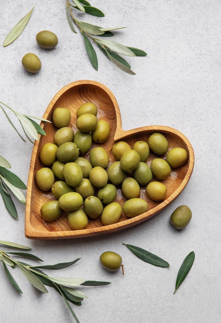 Photo des olives vertes fraîches exposées sur un bol en forme de cœur en bois avec des branches d'olive