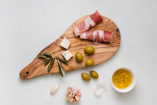 Olives vertes; fromage; ail et bacon sur une planche à découper en bois