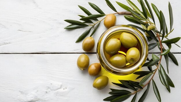 Olives vertes et huile d'olive dans un pot en verre avec une branche d'olivier vue de haut sur une planche en bois blanc