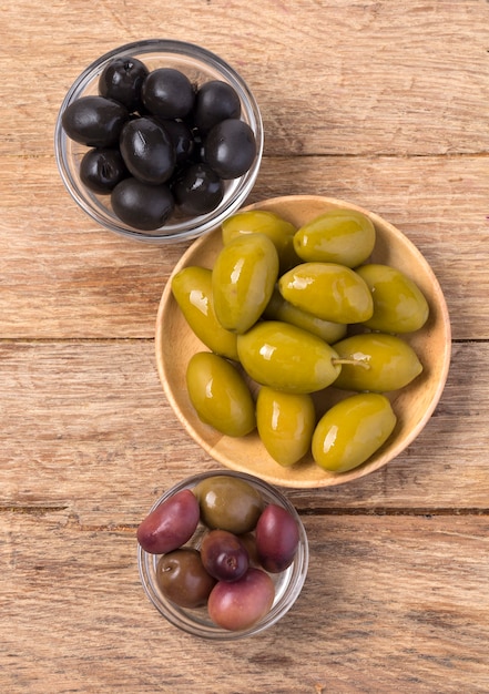 Les olives vertes et noires dans un bol sur fond de bois.