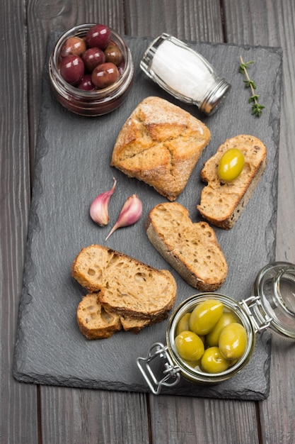 Olives vertes et tranches de pain. Huile d'olive en pot de verre et brins de thym. Mise à plat