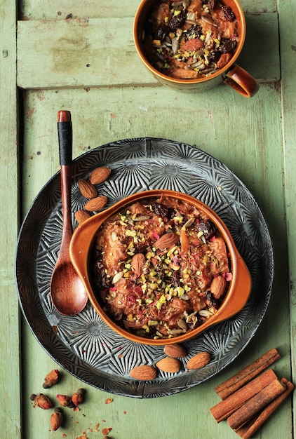 Om Ali ou Um Ali, pain traditionnel arabe ou pudding de croissant avec pistache, amande et pétale de rose comme garniture, dessert lacté et crémeux. Vue de dessus sur fond de bois rustique