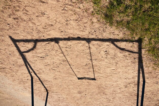 Ombre de la balançoire de l'enfant sur le sable et l'herbe verte à proximité aux beaux jours