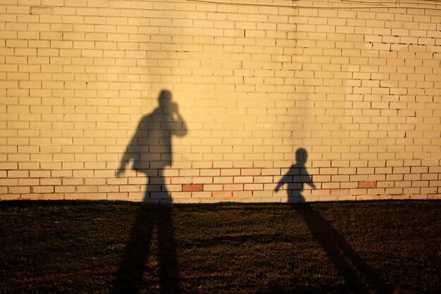 Photo l'ombre d'un homme et d'un garçon sur un mur de briques pendant une journée ensoleillée