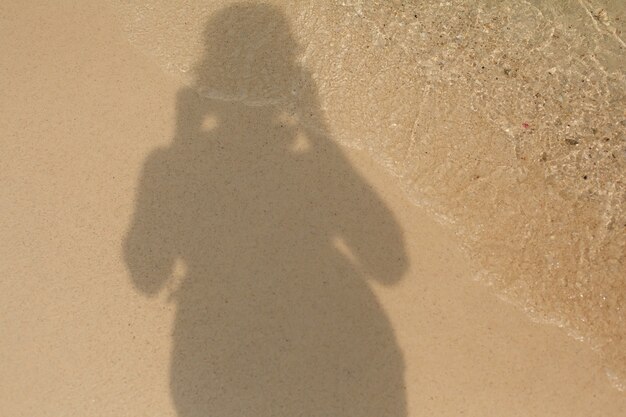 Photo ombre d'un homme sur le rivage sablonneux d'une plage de mer dans les vagues de l'eau