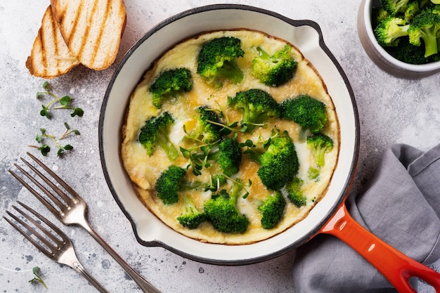 Omelette au brocoli et jeunes oignons verts sur une poêle en fonte rouge sur une vieille table en béton gris. Vue de dessus.