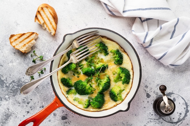 Omelette au brocoli et jeunes oignons verts sur une poêle en fonte rouge sur une vieille table en béton gris. Vue de dessus.