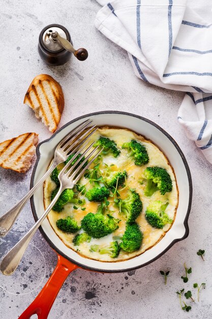 Omelette au brocoli et jeunes oignons verts sur une poêle en fonte rouge sur une vieille table en béton gris. Vue de dessus.