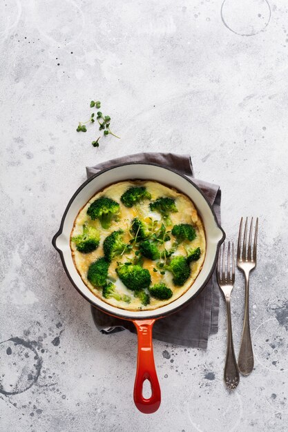Omelette au brocoli et jeunes oignons verts sur une poêle en fonte rouge sur une vieille table en béton gris. Vue de dessus.