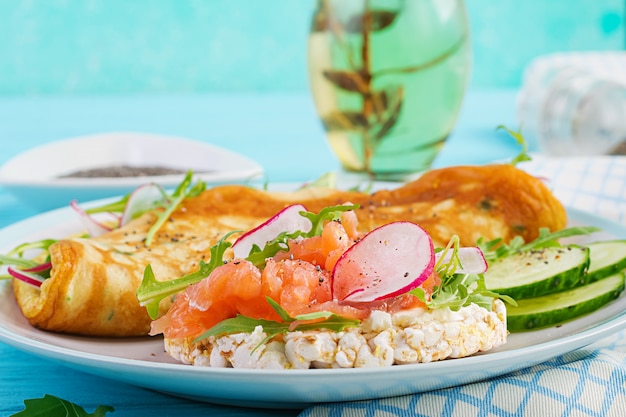 Omelette au radis, roquette verte et sandwich au saumon sur plaque blanche