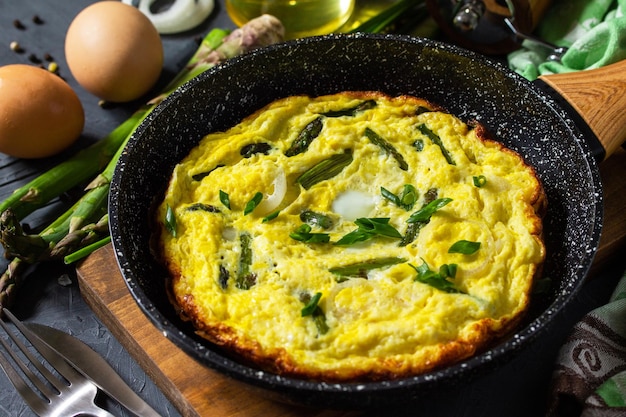 Omelette aux asperges saine Omelette aux œufs avec asperges et oignons dans une poêle en fonte