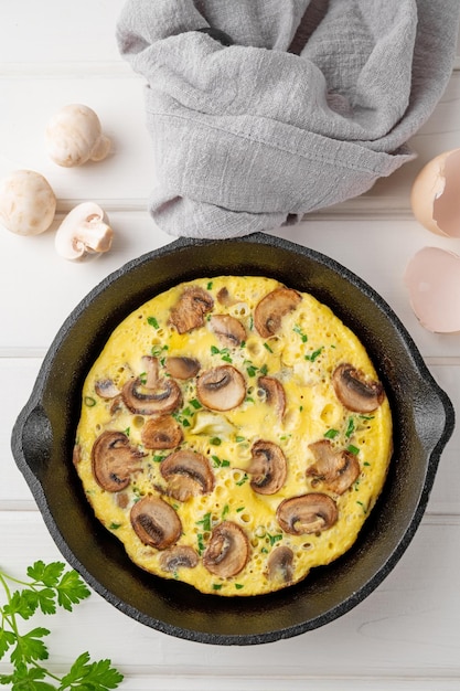 Omelette aux champignons et herbes dans une casserole sur un fond en bois blanc Petit-déjeuner sain