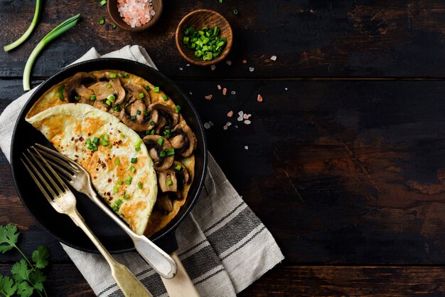 Omelette Aux Champignons Et Jeunes Oignons Verts Sur Une Poêle En Fonte Sur Une Vieille Surface En Bois.