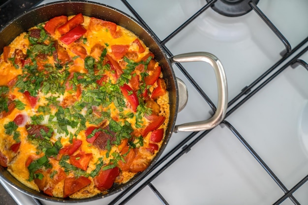 Omelette aux légumes et herbes dans une poêle noire sur une cuisinière blanche.