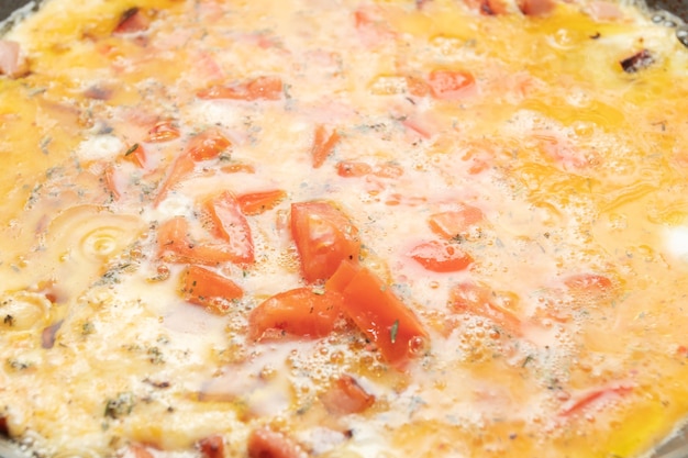 Photo omelette aux œufs avec des tomates et des saucisses pour le petit déjeuner sont frites dans une poêle le matin dans la cuisine