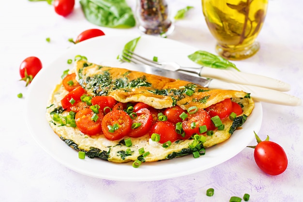 Omelette aux tomates, épinards et oignons verts sur plaque blanche.