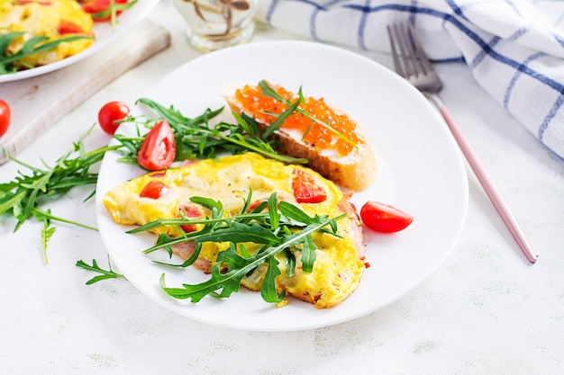 Omelette aux tomates, fromage, jambon et sandwich avec cavier rouge sur assiette. Frittata - omelette italienne.