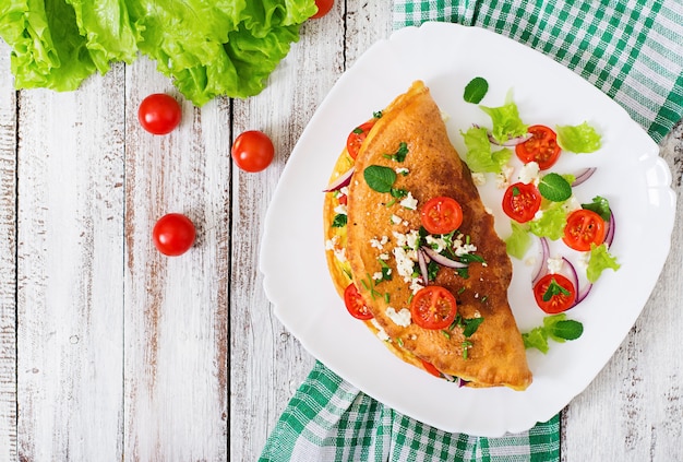 Omelette aux tomates, persil et fromage feta sur plaque blanche. Vue de dessus