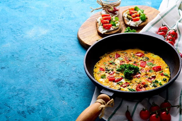 Omelette aux verts et tomates, sandwichs au fromage à la crème, pesto et tomates cerises sur fond turquoise