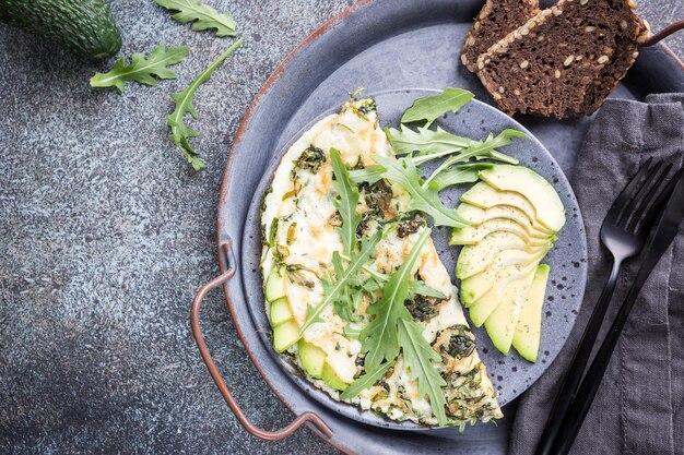 Omelette à l'avocat et à la roquette sur une plaque en céramique grise sur fond de pierre, vue de dessus. Petit-déjeuner sain.