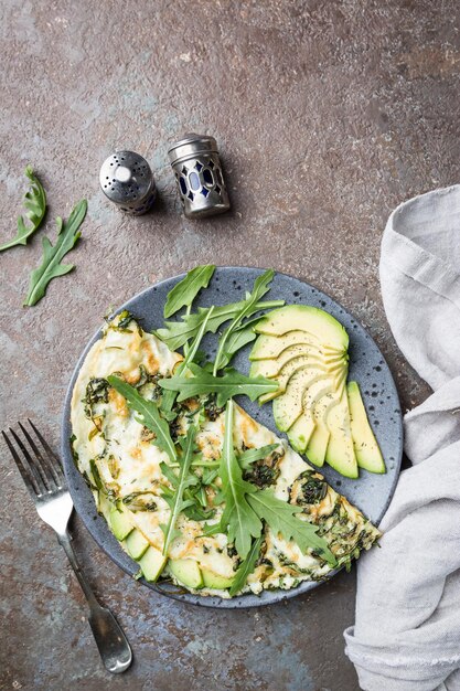 Omelette à l'avocat et à la roquette sur une plaque en céramique grise sur fond de pierre, vue de dessus. Petit-déjeuner sain.