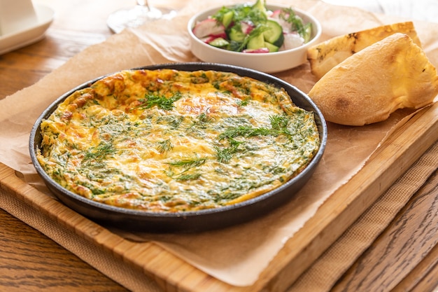 Omelette dans une poêle avec du persil et de l'aneth. Servir avec du pain frais et des légumes frais.