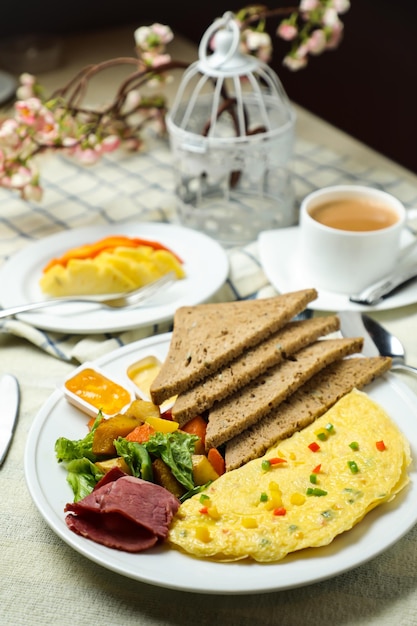 Omelette farcie avec salade de légumes à la viande de pain bown comprend des feuilles de laitue de pomme de terre tomate et des carottes avec du thé, du café et du melon sucré servis sur une table de nourriture, vue de dessus, petit déjeuner sain