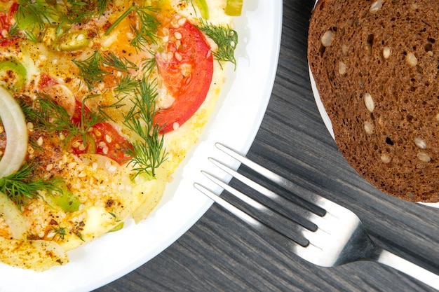 Omelette frite cuite aux herbes et légumes dans une assiette blanche sur une table en bois