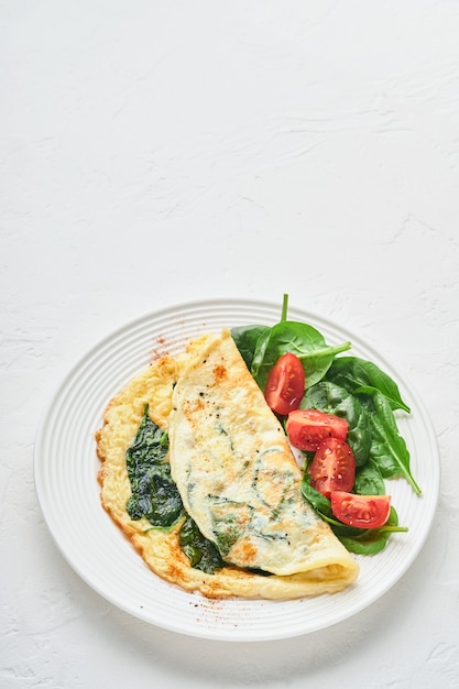 Omelette ou omelette aux épinards, tomate cerise et assaisonnement au poivre sur une plaque blanche, sur fond blanc. Vue de dessus.