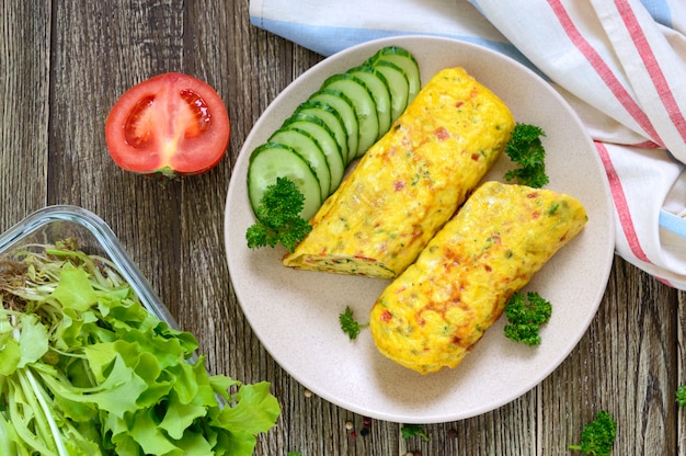 Omelette, rouleau d'oeufs aux légumes et herbes sur une table en bois. Délicieux petit déjeuner sain. Vue de dessus.