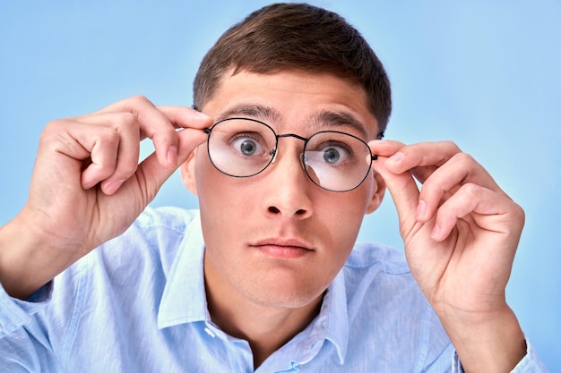 OMG Studio tourné un homme caucasien choqué tient les mains sur le bord des lunettes ne peut pas croire que ses yeux regardent avec curiosité la réaction émotionnelle de la caméra à des nouvelles inattendues isolées sur fond bleu