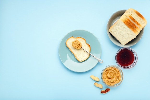 Photo Сooking petit déjeuner tartiner du pain, des toasts au beurre d'arachide, pâte d'arachide crémeuse sur fond bleu