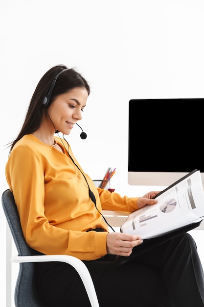 opérateur téléphonique caucasien femme portant un casque de microphone tenant des tableaux et des graphiques en papier tout en travaillant au bureau