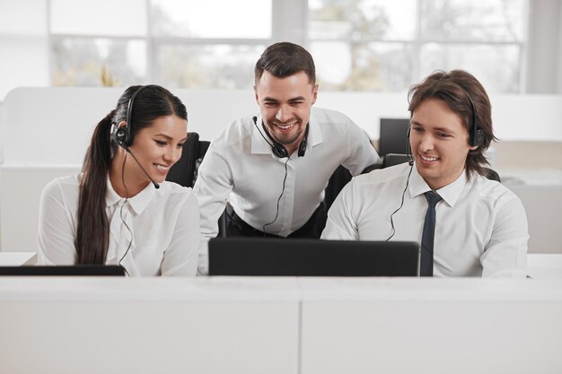 Opérateurs de centre d'appels souriants discutant et partageant un ordinateur au bureau