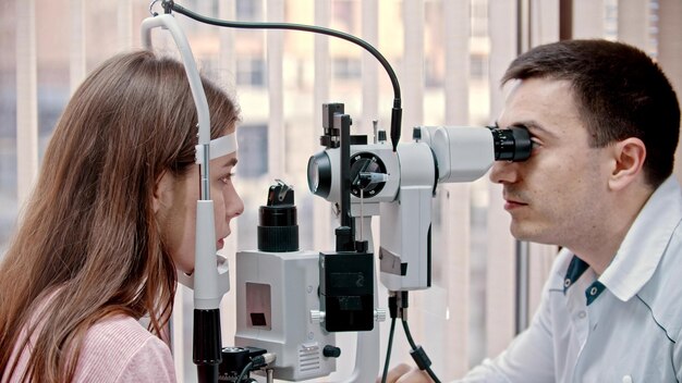 Ophtalmologie à l'intérieur d'un médecin vérifiant l'acuité visuelle de la jeune femme avec une machine spéciale une armoire spacieuse avec fenêtre panoramique avec stores