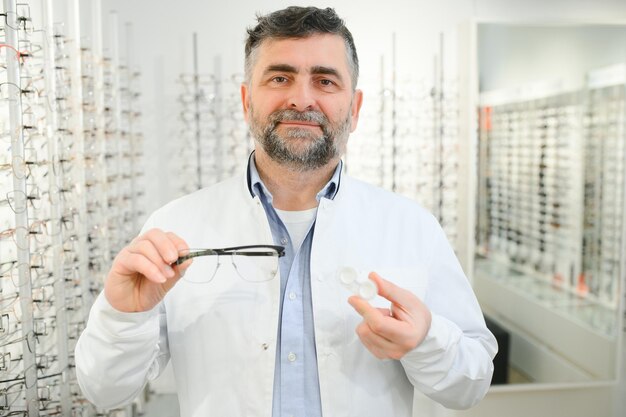 Ophtalmologiste choisissant entre des lunettes et des lentilles debout devant le tableau des yeux dans l'armoire