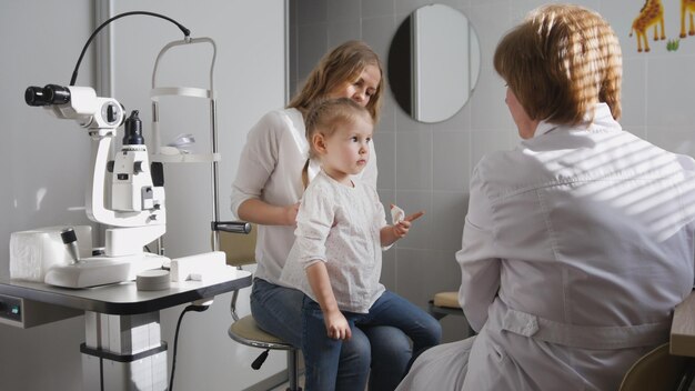 L'ophtalmologiste en clinique explique le diagnostic de la vue de la fille - l'enfant joue, horizontal