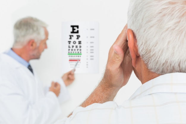 Ophtalmologiste pédiatre avec un patient senior pointant au tableau de l&#39;oeil