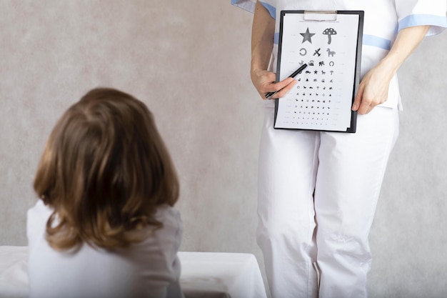 L'ophtalmologiste vérifie la vision d'un garçon de 5 ans au moyen d'un tableau des yeux pour les enfants.