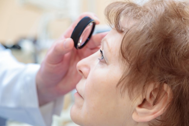 Un ophtalmologue masculin examine la vue d'une femme adulte à l'aide d'un ophtalmoscope binoculaire