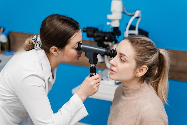 Ophtalmoscopie L'ophtalmologiste examine les yeux d'une femme avec un ophtalmoscope Consultation d'ophtalmologie avec un optométriste dans une clinique médicale