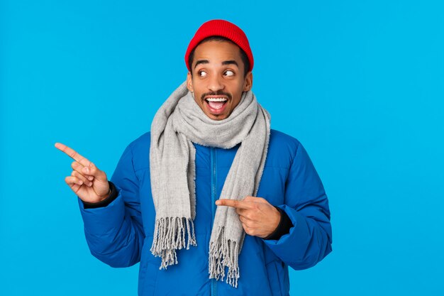 Optimiste, amusé et joyeux homme afro-américain en veste rembourrée, écharpe d'hiver et bonnet