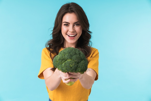 optimiste positive jeune belle femme posant isolée sur mur bleu tenant le brocoli.