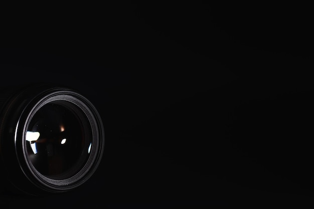 Optique à la caméra sur le bureau de l'opérateur. Éclat dans le verre d'un objectif photo. Fond noir avec la technique du photographe.