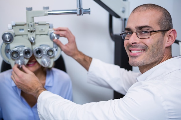 Optométriste souriant examinant une patiente sur un réfracteur