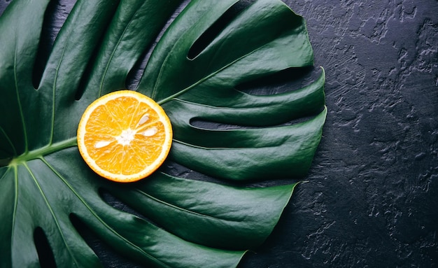 Une orange sur une feuille tropicale verte. Plante d'intérieur Monstera sur fond noir. Photo écologique.