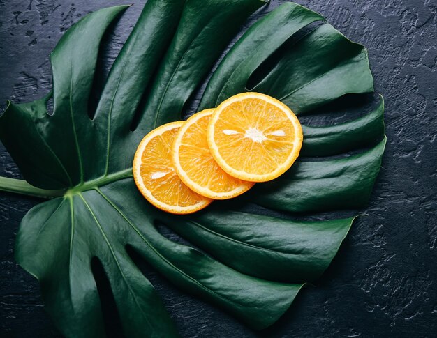 Une orange sur une feuille tropicale verte. Plante d'intérieur Monstera sur fond noir. Photo écologique.